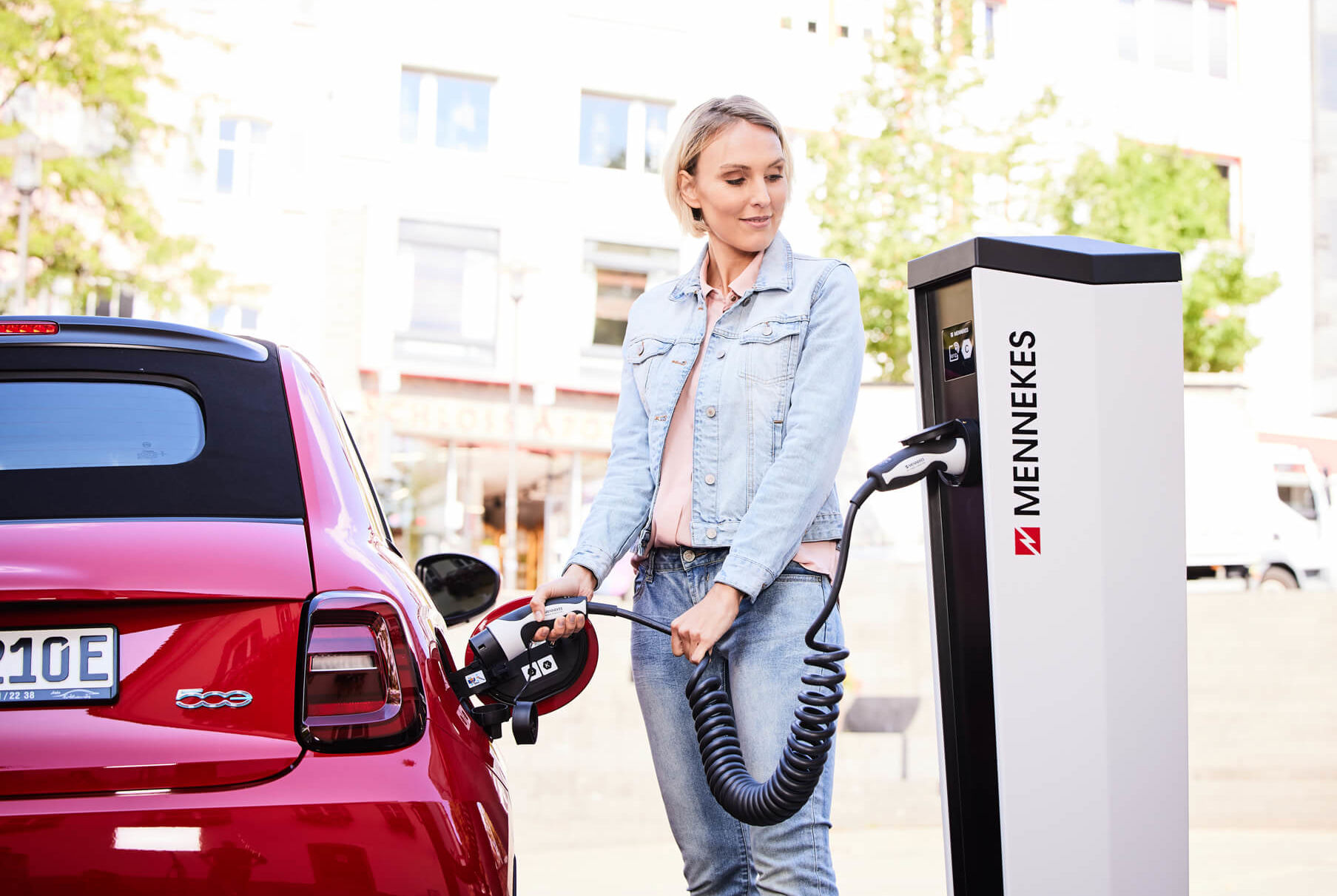 Eine Frau nutzt ein spiralisierte Typ2 Ladekabel um Ihr Elektroauto an einer öffentlichen Ladesäule anzuschließen